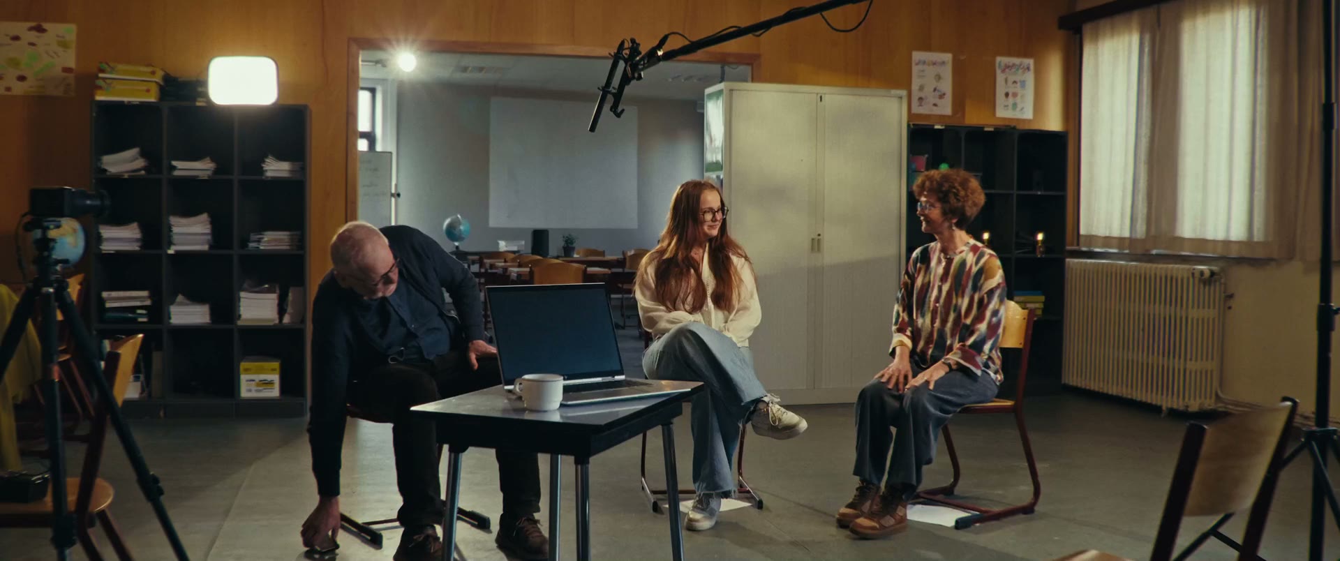 De filmploeg in gesprek: een interviewer zit tegenover twee leerlingen in een klaslokaal, met micro en camera in beeld.